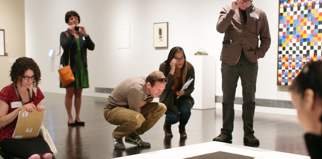 A group with clipboards examines an artwork on the ground