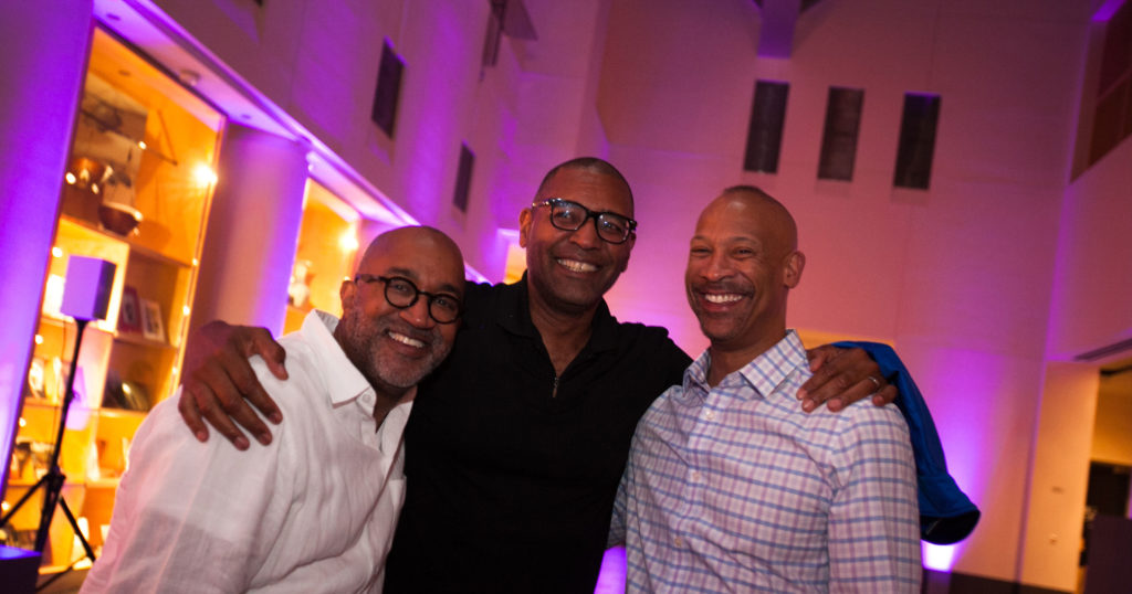 Three men in business-casual attire embracing and smiling