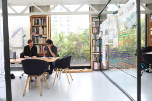 Tatiana Bilbao and a colleague work together at a table in a nicely designed office space with architectural drawings on the walls.